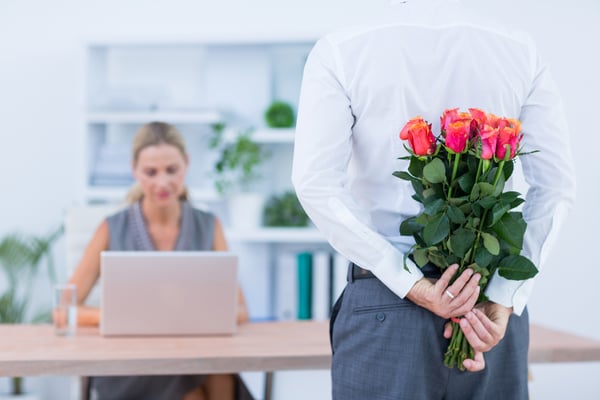 Businessman hiding flowers behind back for colleague in the office