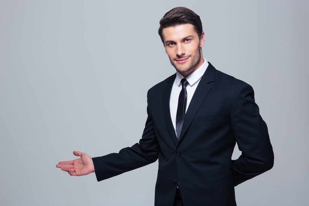 Businessman with arm out in a welcoming gesture over gray background.jpeg