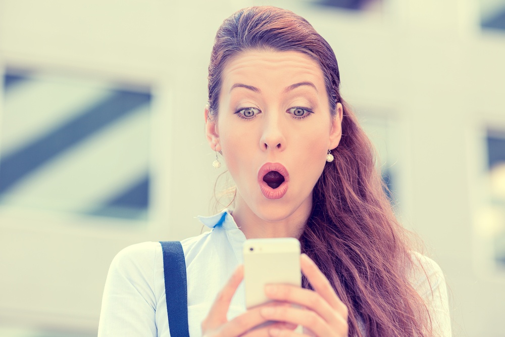 Closeup portrait anxious young girl looking at phone seeing bad news or photos with disgusting emotion on her face isolated outside city background. Human emotion, reaction, expression .jpeg